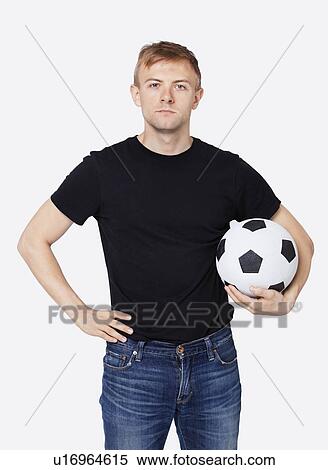 Stock Photography - Portrait of a young handsome man in casual wear holding soccer ball over white background. Fotosearch