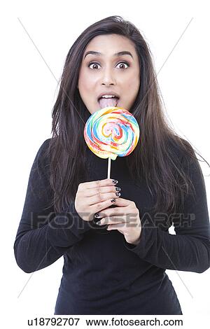 Stock Photo - Portrait of a young indian woman licking a multi-colored lollipop. Fotosearch