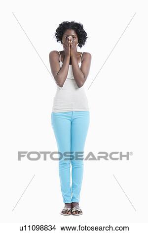 Picture - Portrait of an amazed young woman with hands over mouth standing against white background. Fotosearch