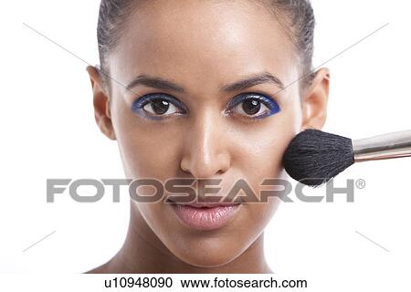 Stock Image - Portrait of beautiful young woman applying makeup against white background. Fotosearch