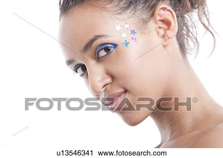 Stock Image - Portrait of beautiful young woman with blue eyeshadow and stars on face against white background. Fotosearch