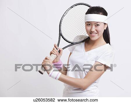 Stock Image - Portrait of happy female tennis player holding racket against white background. Fotosearch