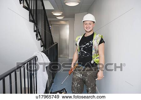 Portrait of happy young construction worker standing by railing View Large Photo Image Stock Photo - Portrait of happy young construction worker standing by railing. Fotosearch