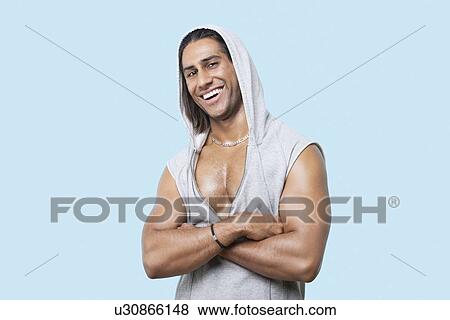Stock Photo - Portrait of happy young muscular man with arms crossed standing against blue background. Fotosearch