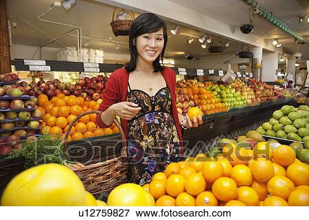 Portrait of happy young woman holding orange with basket in market View Large Photo Image Stock Photo - Portrait of happy young woman holding orange with basket in market. Fotosearch