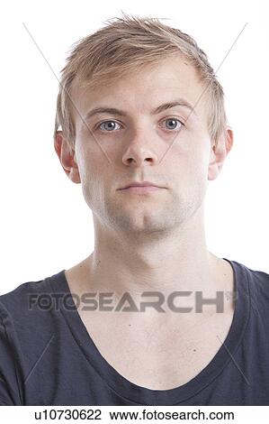 Stock Image - Portrait of serious young man in blue tshirt against white background. Fotosearch