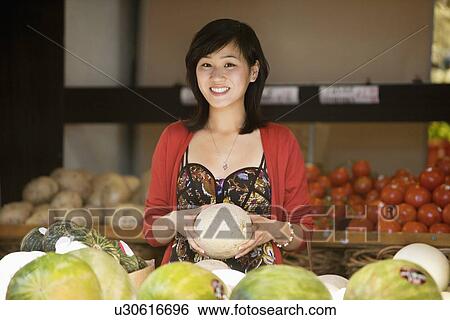 Portrait of smiling young woman holding melon in market View Large Photo Image Stock Photograph - Portrait of smiling young woman holding melon in market. Fotosearch