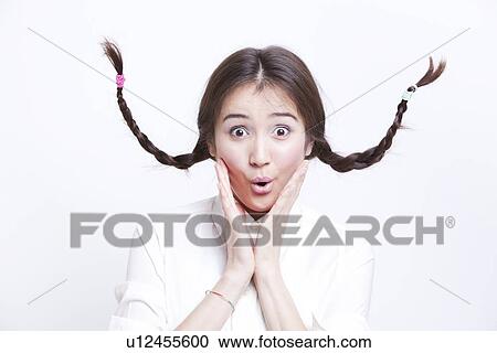 Stock Image - Portrait of surprised young woman with braids curling upwards against white background. Fotosearch