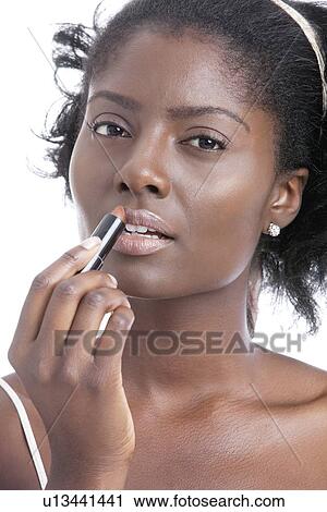 Stock Image - Portrait of young African American woman applying lipstick. Fotosearch