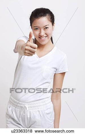 Stock Photo - Portrait of young Asian woman gesturing thumbs up against white background. Fotosearch