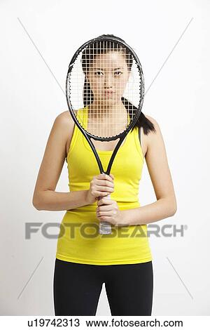 Portrait of young Asian woman holding tennis racket in front of her face against white background View Large Photo Image Stock Image - Portrait of young Asian woman holding tennis racket in front of her face against white background. Fotosearch