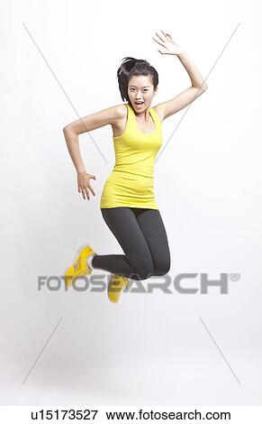 Stock Photo - Portrait of young Asian woman in yellow tank top and leggings jumping against white background. Fotosearch