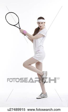 Stock Photography - Portrait of young Caucasian with tennis racket standing on one leg against white background. Fotosearch
