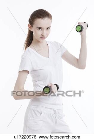 Stock Photograph - Portrait of young Caucasian woman exercising with dumbbells against white background. Fotosearch