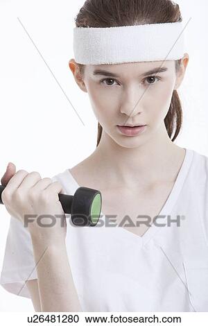 Stock Image - Portrait of young Caucasian woman with dumbbell against white background. Fotosearch