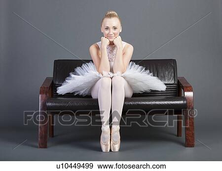 Stock Photo - Portrait of young female ballet dancer sitting on sofa over grey background. Fotosearch