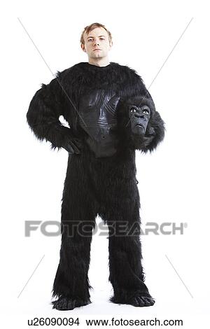 Picture - Portrait of young man in gorilla costume with hand on hip against white background. Fotosearch