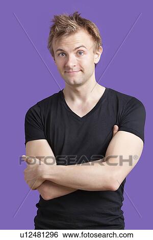 Stock Photograph - Portrait of young man with arms crossed standing against violet background. Fotosearch