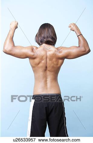 Portrait of young muscular man flexing his arms standing over light blue background with back to camera View Large Photo Image Stock Photo - Portrait of young muscular man flexing his arms standing over light blue background with back to camera. Fotosearch