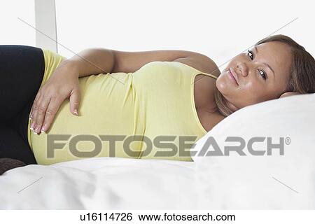 Stock Photograph - Portrait of young pregnant woman relaxing on bed at home. Fotosearch