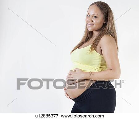 Portrait of young pregnant woman with hands on stomach against white background View Large Photo Image Stock Photo - Portrait of young pregnant woman with hands on stomach against white background. Fotosearch