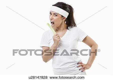 Stock Photo - Portrait of young sportswoman eating celery over white background. Fotosearch