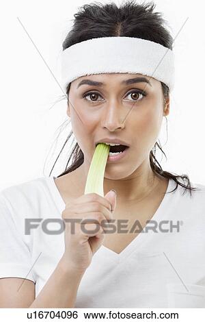 Stock Photograph - Portrait of young sportswoman eating celery over white background. Fotosearch