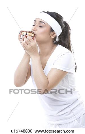 Stock Image - Portrait of young sportswoman enjoying a donut over white background. Fotosearch