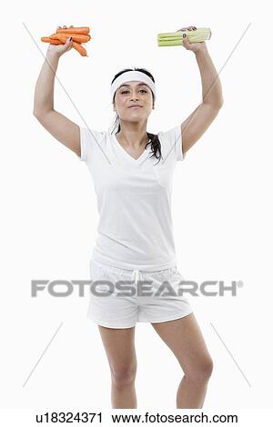 Portrait of young sportswoman with arms raised holding carrots and celery over white background View Large Photo Image Stock Image - Portrait of young sportswoman with arms raised holding carrots and celery over white background. Fotosearch