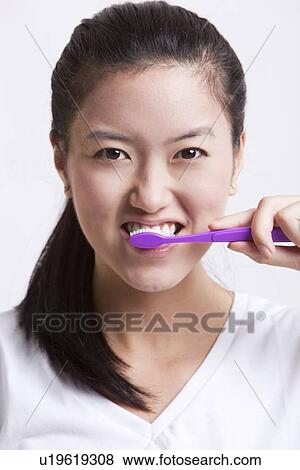 Portrait of young woman brushing her teeth against white background View Large Photo Image Stock Photo - Portrait of young woman brushing her teeth against white background. Fotosearch