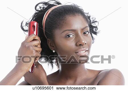 Stock Image - Portrait of young woman combing her hair with hairbrush over white background. Fotosearch