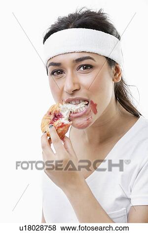 Stock Photo - Portrait of young woman eating donut over white background. Fotosearch