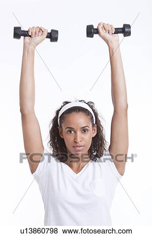 Stock Photo - Portrait of young woman exercising with dumbbells against white background. Fotosearch