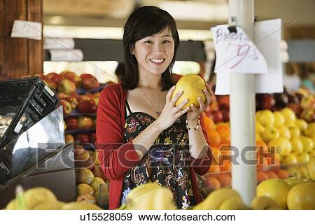 Stock Photo - Portrait of young woman holding fruit in market. Fotosearch