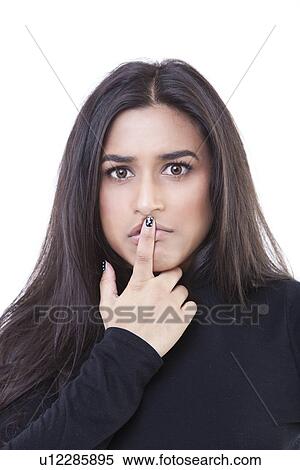 Stock Photography - Portrait of young woman holding her finger to her lips against white background. Fotosearch