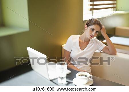 Stock Photograph - Portrait of young woman sitting at table with laptop in cafe. Fotosearch