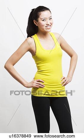 Stock Photo - Portrait of young woman smiling with hands on hips against white background. Fotosearch