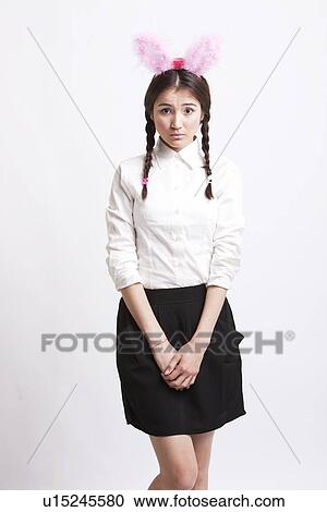 Stock Image - Portrait of young woman with bunny ears against white background. Fotosearch
