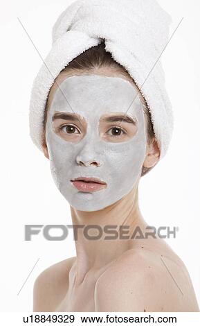 Stock Photo - Portrait of young woman with face pack and towel wrapped around head against white background. Fotosearch