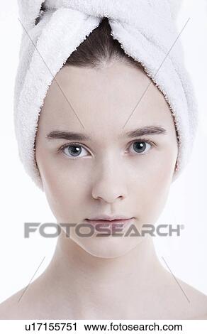 Stock Image - Portrait of young woman with towel wrapped around her head against white background. Fotosearch