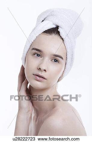 Stock Image - Portrait of young woman with towel wrapped around her head against white background. Fotosearch