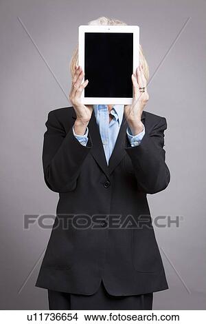 Picture - Senior businesswoman holding tablet up to her face. Fotosearch