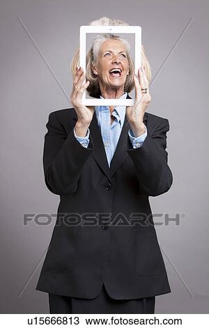 Stock Image - Senior businesswoman holding tablet up to her face showing another face on her tablet . Fotosearch