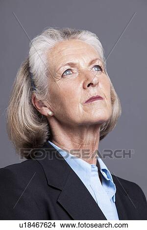 Picture - Senior businesswoman looking upwards a grey background. Fotosearch