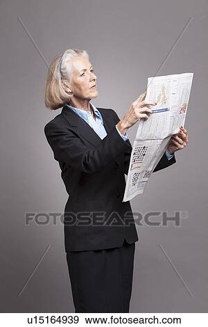 Stock Photo - Senior businesswoman reading news paper on grey background. Fotosearch