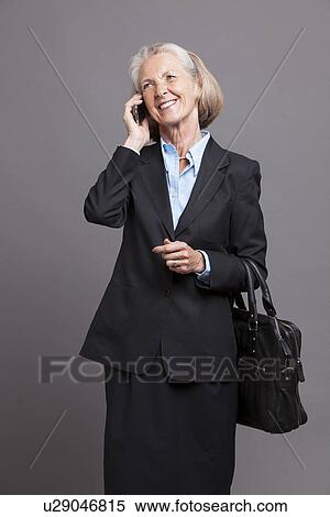Stock Photography - Senior businesswoman using smart phone to make a phone call on grey background. Fotosearch