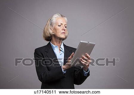 Senior businesswoman using tablet on grey background View Large Photo Image Stock Image - Senior businesswoman using tablet on grey background. Fotosearch