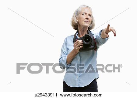 Senior female photographer with camera gesturing against white background View Large Photo Image Stock Image - Senior female photographer with camera gesturing against white background. Fotosearch