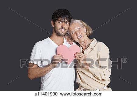 Senior woman and young man holding red paper heart against black background View Large Photo Image Stock Image - Senior woman and young man holding red paper heart against black background. Fotosearch