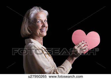 Stock Photography - Senior woman holding heart-shaped cardboard. Fotosearch